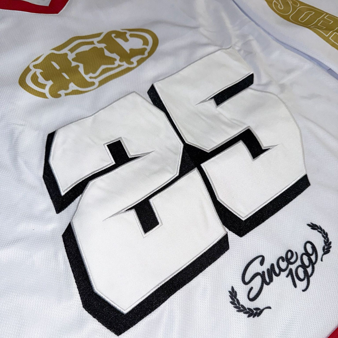 The 2025 Oversized Hockey Racer Jersey is a white sports jersey featuring a bold black-and-white number 25, a gold emblem above it, and "Since 1999" in black script with laurel leaves below.