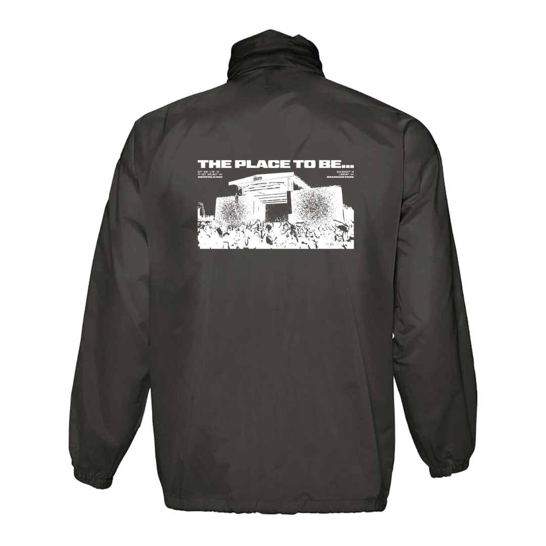 A black Reading & Leeds Festival Rain Coat featuring bold white text THE PLACE TO BE... on the back above a building and crowd graphic. Perfect festival jacket for all-weather protection and style.