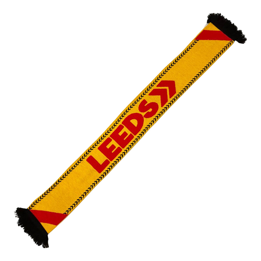 The Leeds Scarf by Reading & Leeds Festival is yellow with bold red LEEDS lettering, black fringe, red diagonal stripes at each end, and a striking black chevron pattern along the edges.